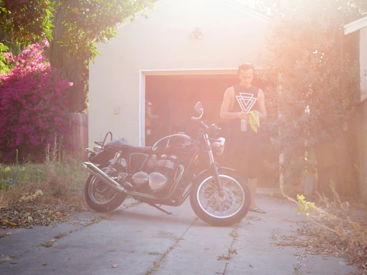 man stands behind motorcycle parked in front of a garage