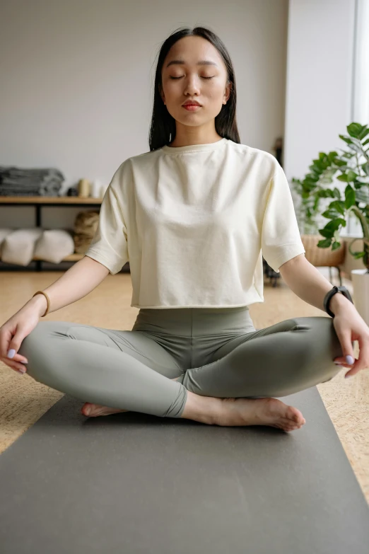 a woman in white shirt sitting on yoga mat with legs crossed and eyes closed