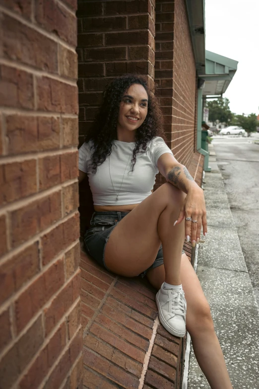 a young woman sits on the ledge of a brick building