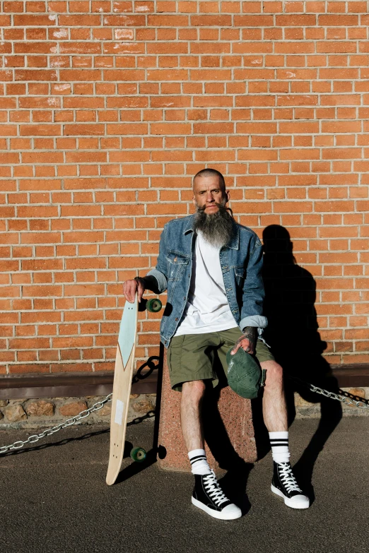 a man sitting in front of a brick wall holding a skateboard