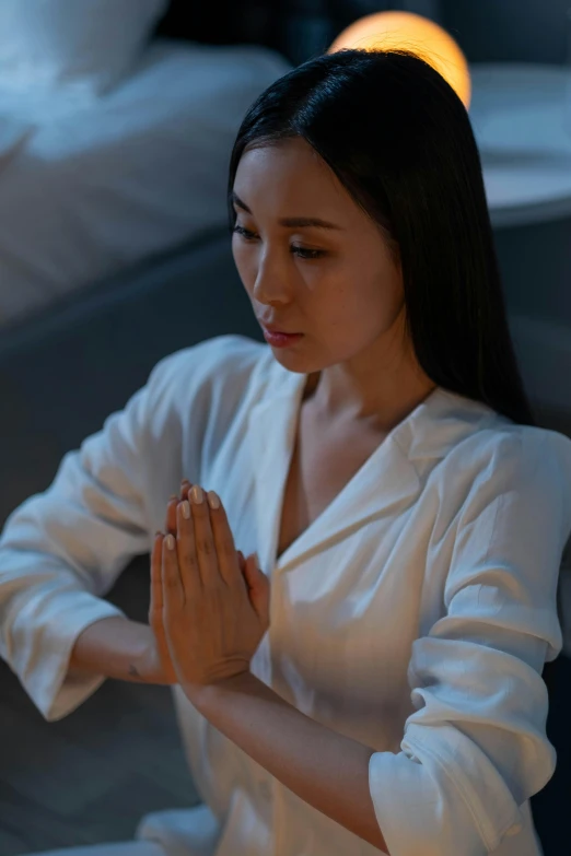 a woman in a white dress praying with her hands clasped