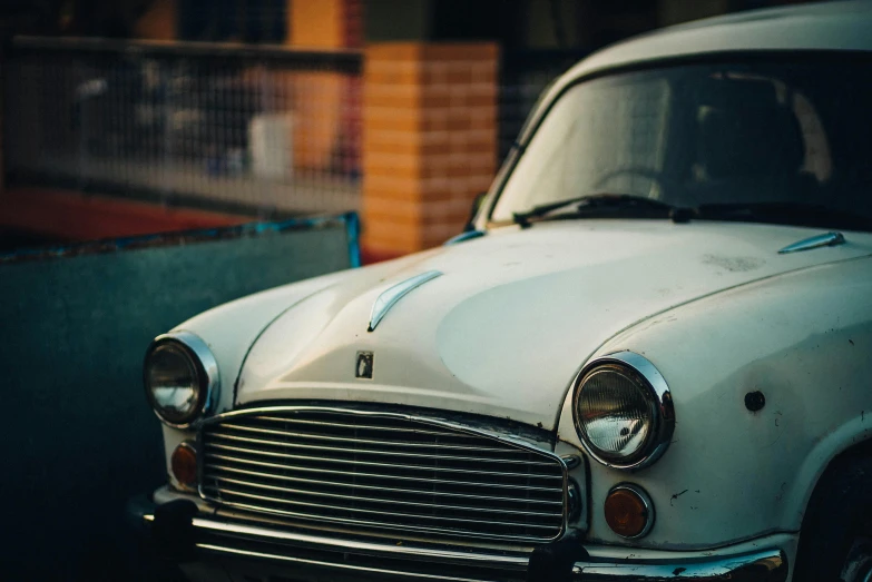 an old white car sits parked beside a brick building