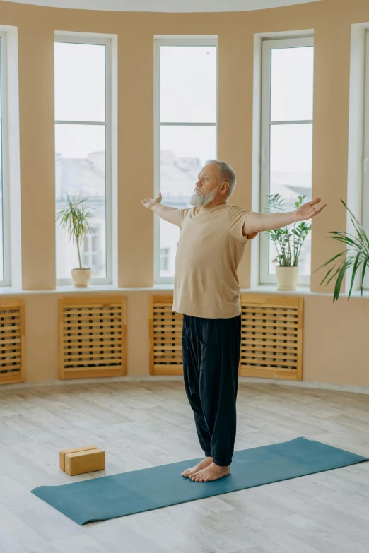 the elderly man is practicing yoga in a room with windows