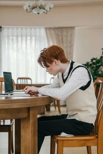 a woman in white sweater sitting at a wooden table with a laptop