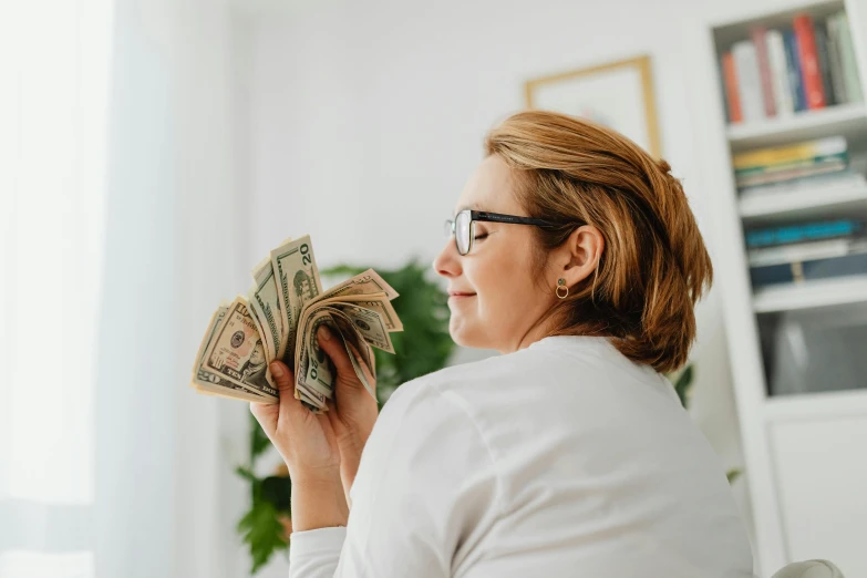 a woman in glasses holding money and looking away