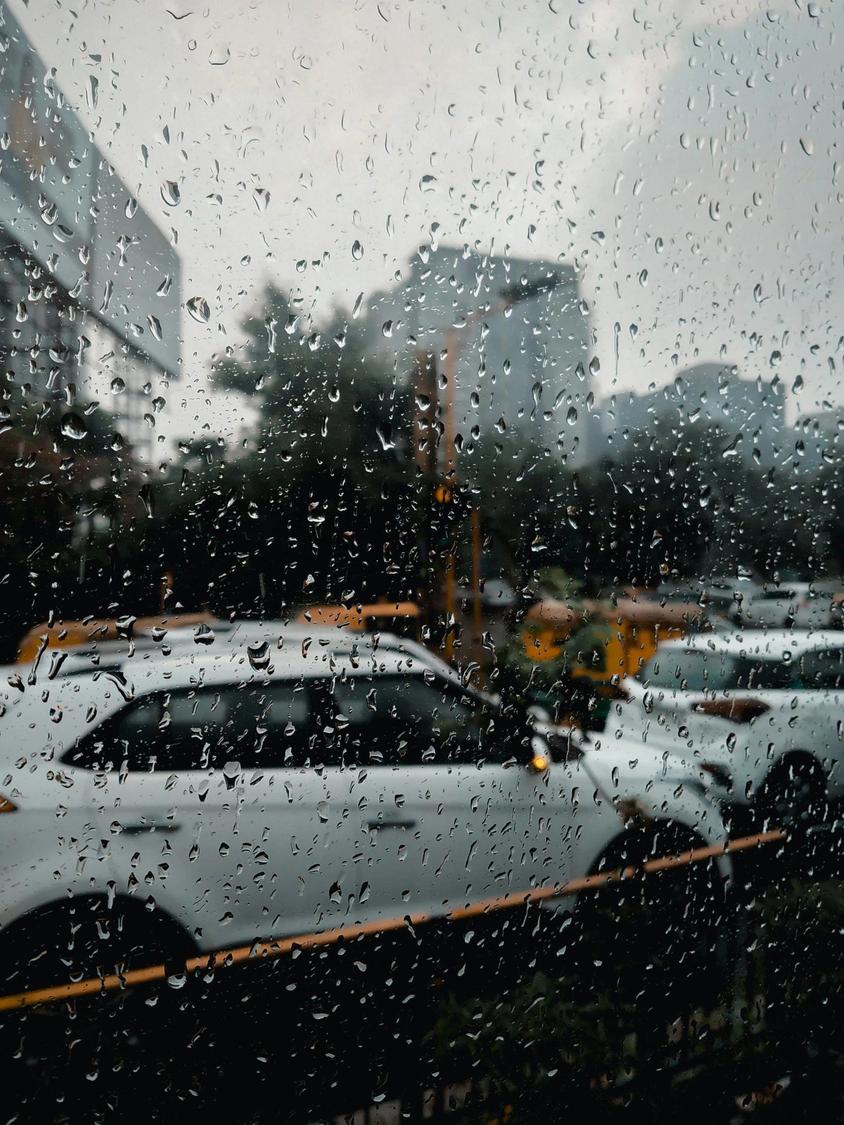 a rainy window that shows cars on the road and buildings in the background