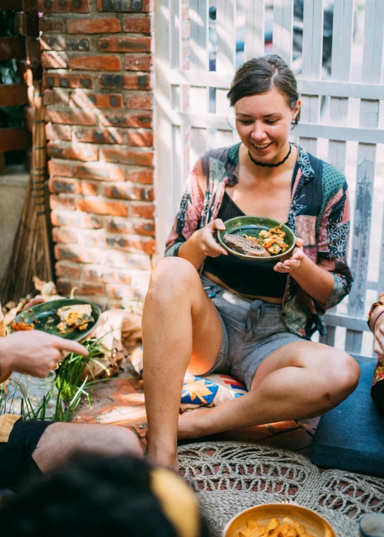 a woman sitting down on the ground eating dinner from a plate