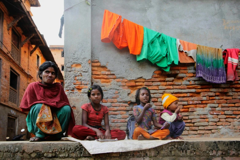 three young indian girls sitting on a wall with drying clothes in the background