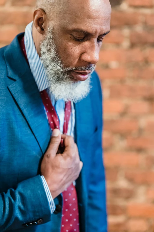 man in blue suit looking down while adjusting tie