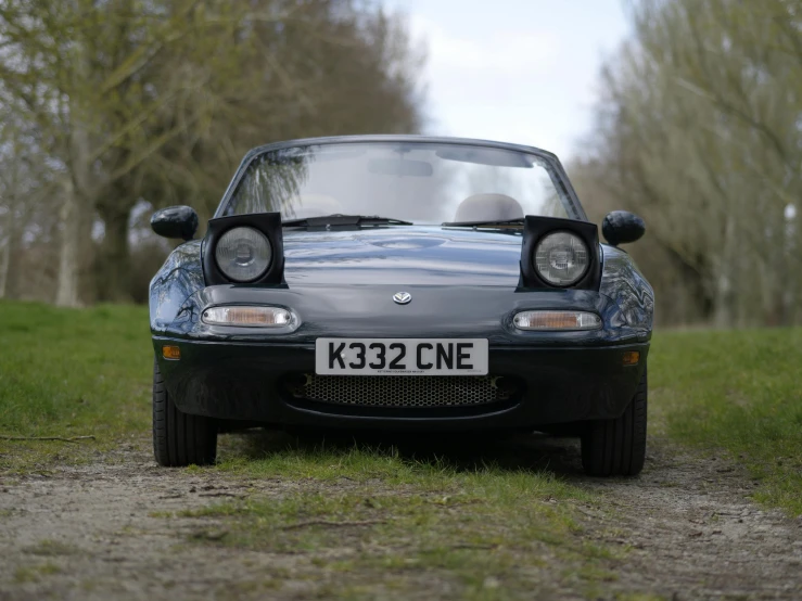 the front end of a gray car parked on a gravel road