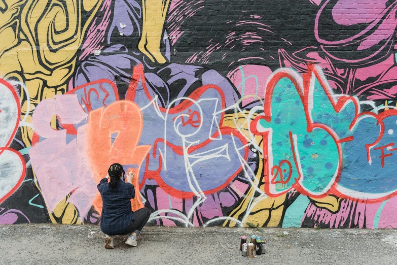 a person squatted in front of a wall with graffiti on it