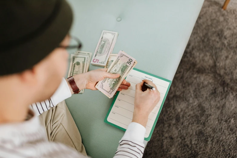 a person writing on a notebook with several bills