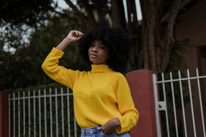 a woman in a yellow sweater is standing near a fence