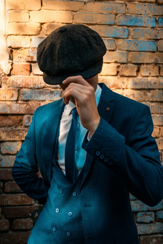 man covering his face with his hand in front of brick wall