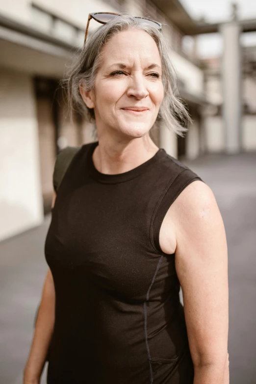 an older woman stands in a courtyard smiling