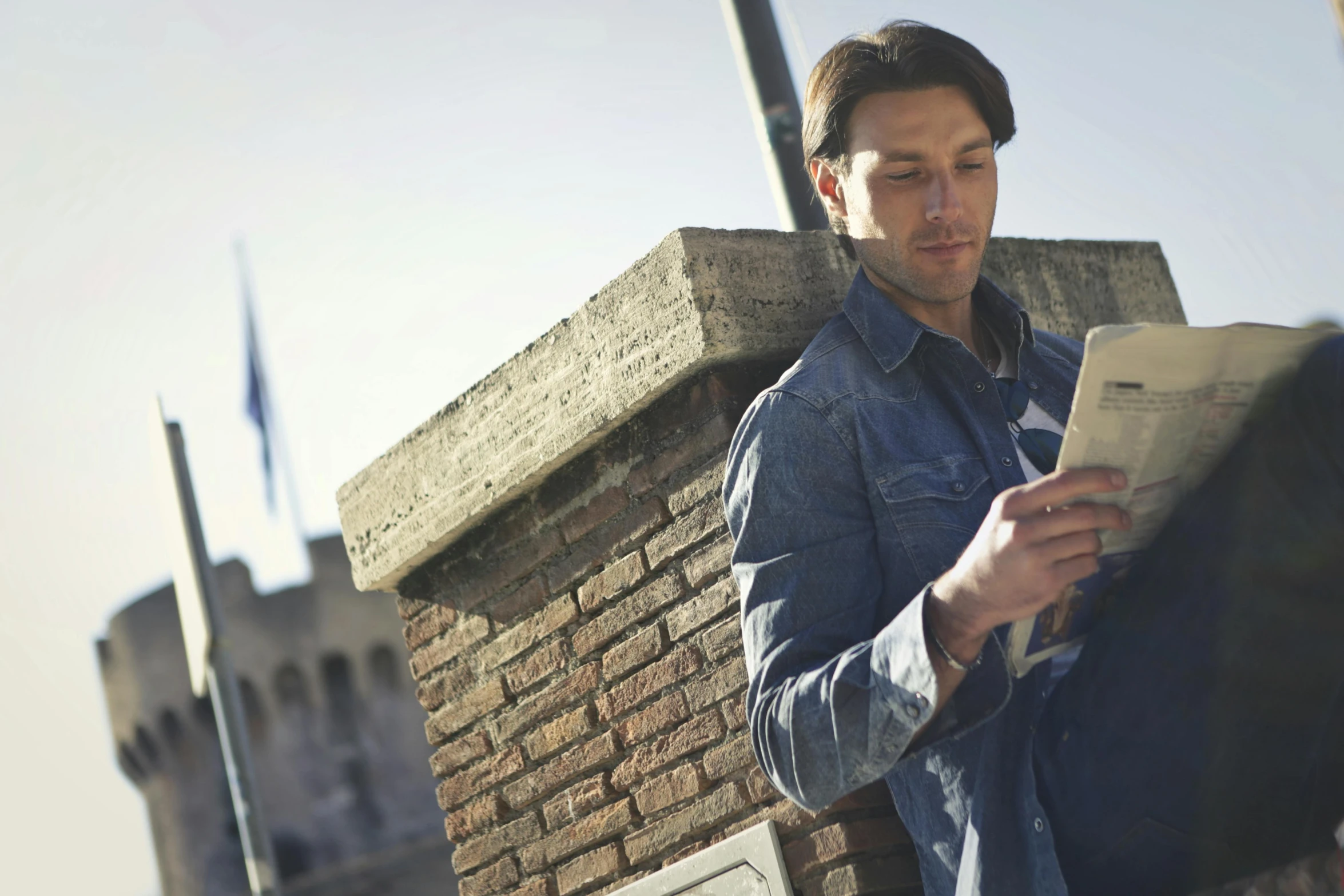 man reading a newspaper while sitting on the side of a building