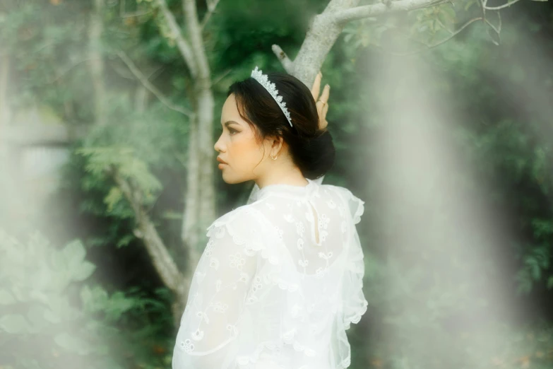 a lady in a veil, standing next to a tree