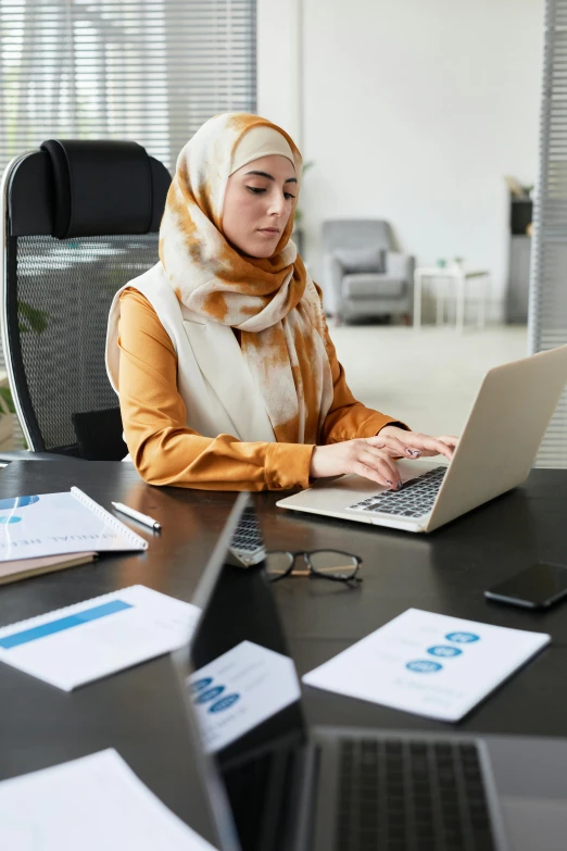 a woman sits at a desk on her laptop and is typing on the keyboard