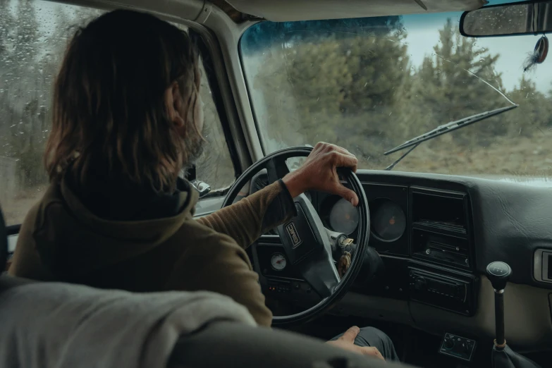 woman driving car through rain covered woods with trees