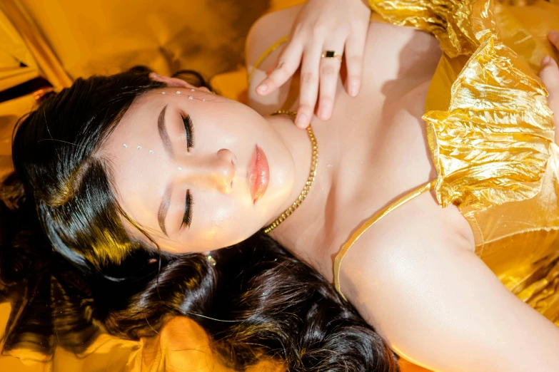 a woman wearing a shiny gold dress laying on a bed