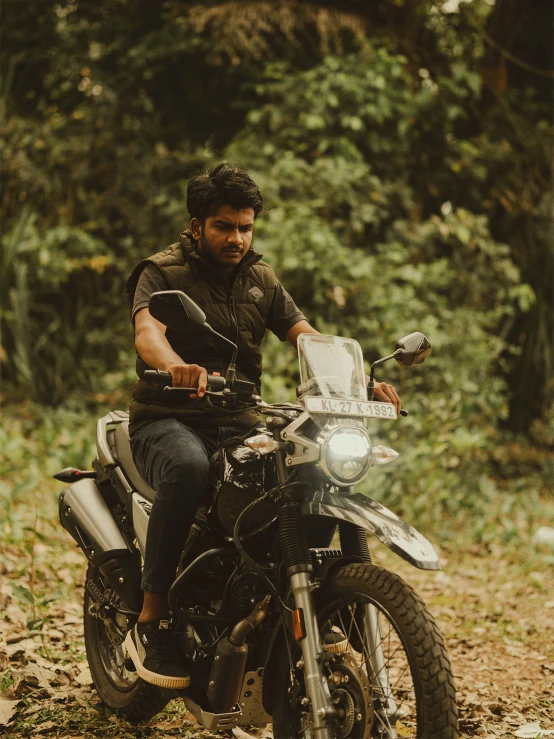 the man is sitting on a motorcycle near some trees