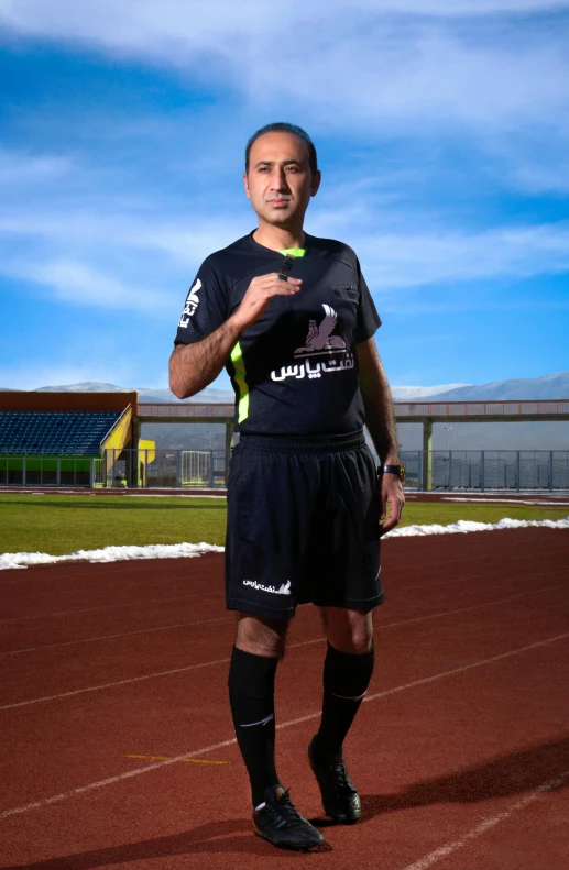 man standing on a track in soccer jersey holding a soccer ball