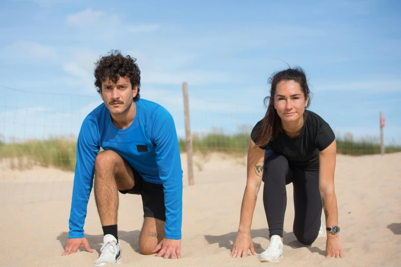 a woman crouches down while a man squats behind her on the sand