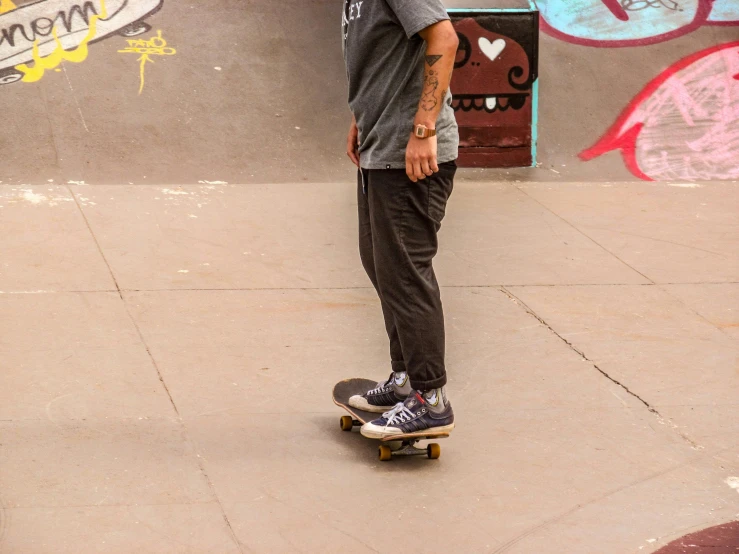 a skateboarder wearing grey pants standing near the edge of a skateboard ramp