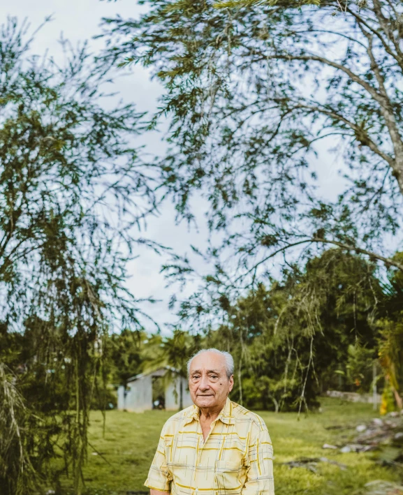 an old man standing in the grass with trees and plants in the background
