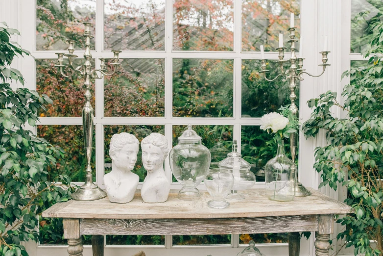 table with vases, bottles, and plants with flowers in glass jars sitting on a windowsill