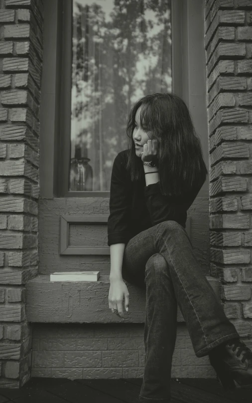 black and white image of woman sitting on a window sill holding a cup of coffee