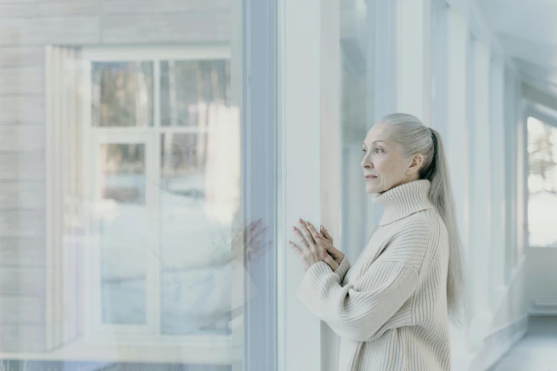 the old lady is standing near the window and making a gesture