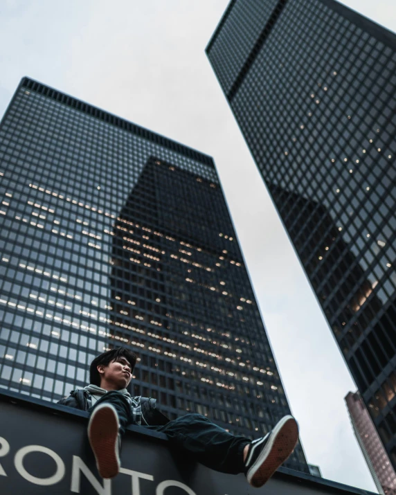 man sitting on sign with large city buildings in the background