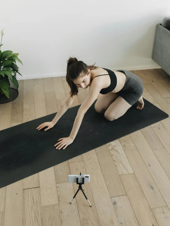 a woman in tight clothing kneeling on a mat and taking a picture with a phone