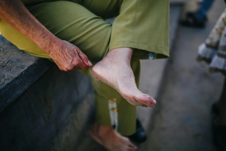 an older person with bare feet sits on a stone bench