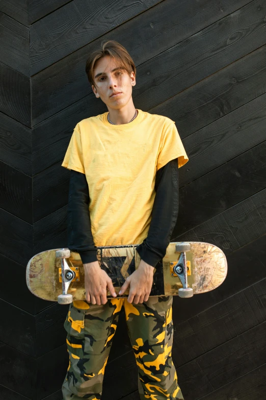 a young man holding a skateboard against a wall