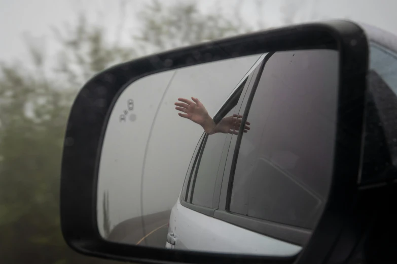 hand coming out the back window of a car that is outside