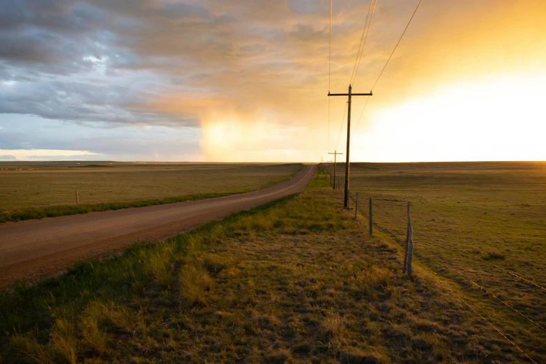 a dusty country road with some power lines at sunset