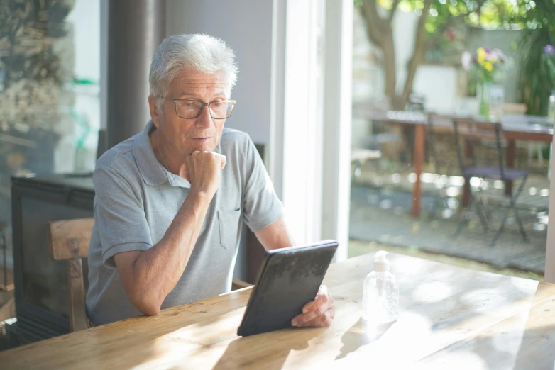 man with eyeglasses looking at tablet screen while sitting outside