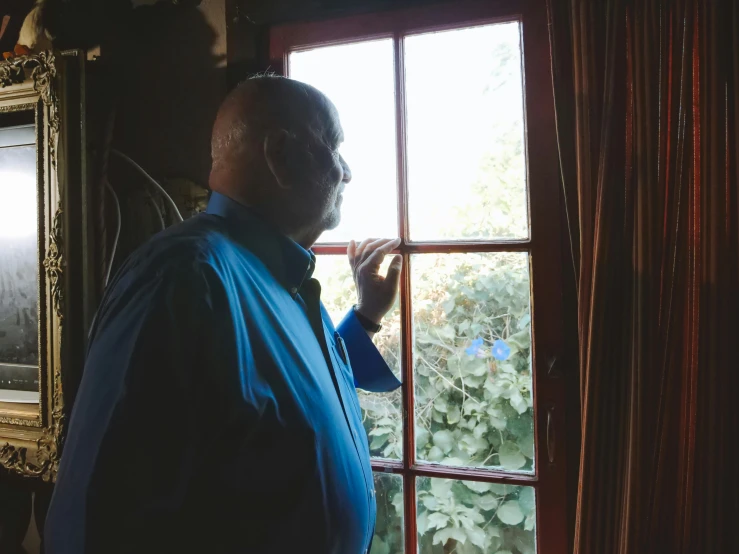 an old man in a blue jacket is looking out a window