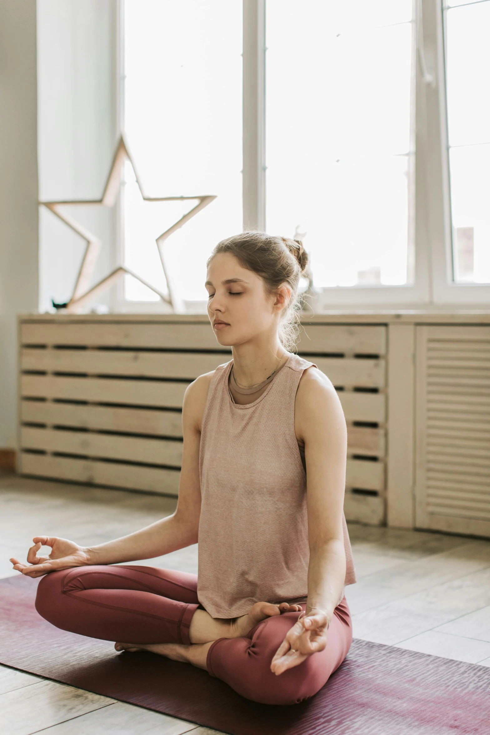 a woman in a beige tank top and red pants practicing yoga