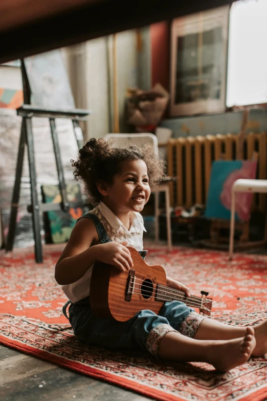 a young child is sitting on the floor and playing the ukulele