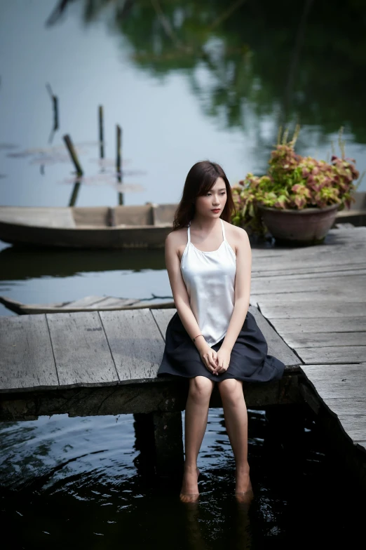 a lady sitting on a dock wearing a skirt and a tank top