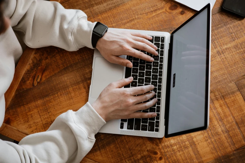 someone typing on a laptop with a wooden table