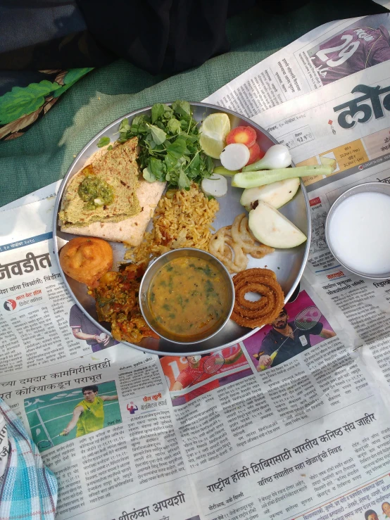 a metal plate filled with food sitting on top of a newspaper