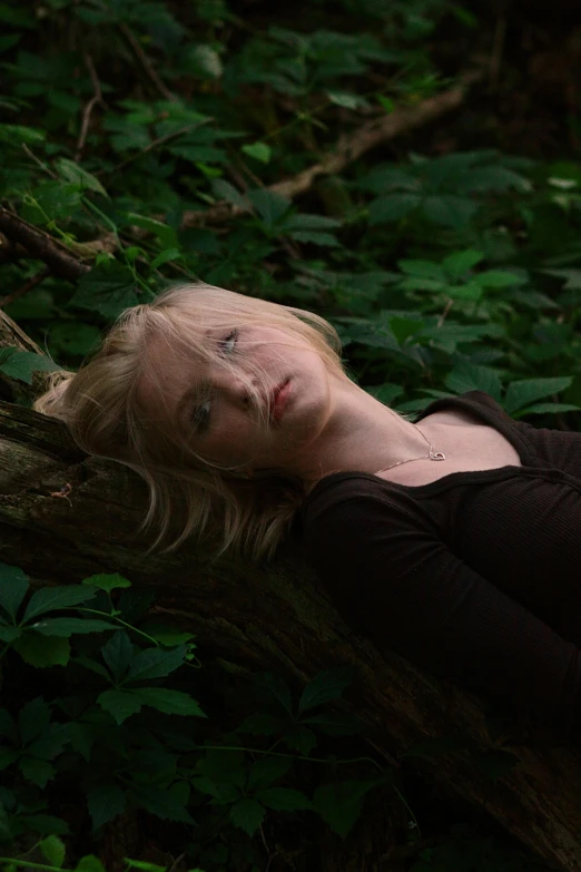 a woman with blond hair laying on a tree nch in the woods