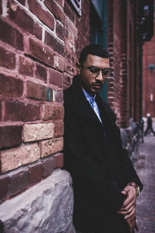 a man standing next to a brick wall wearing a suit and tie