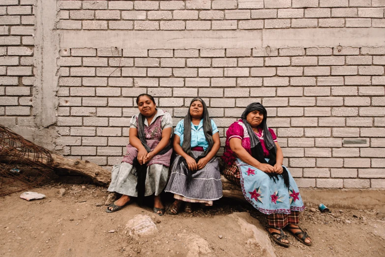 three women sit in front of a brick wall