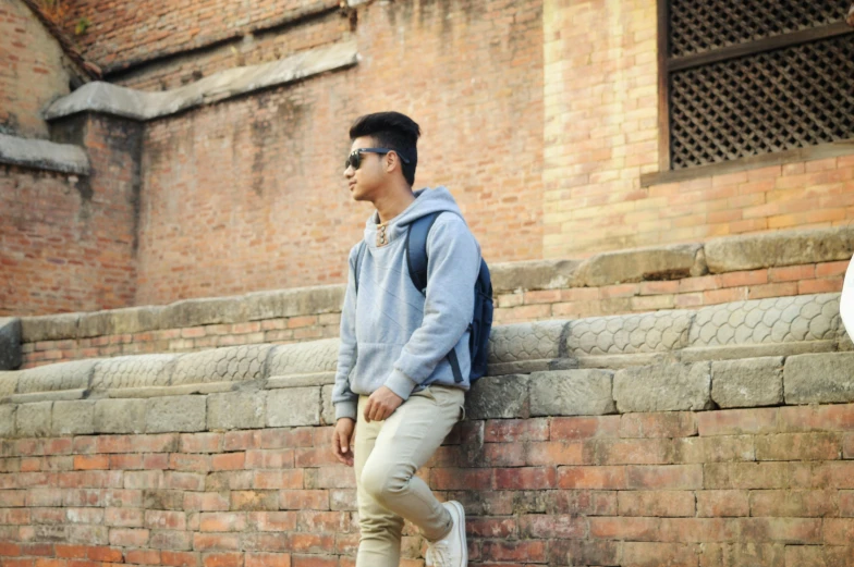 a man is leaning against a brick wall with a backpack