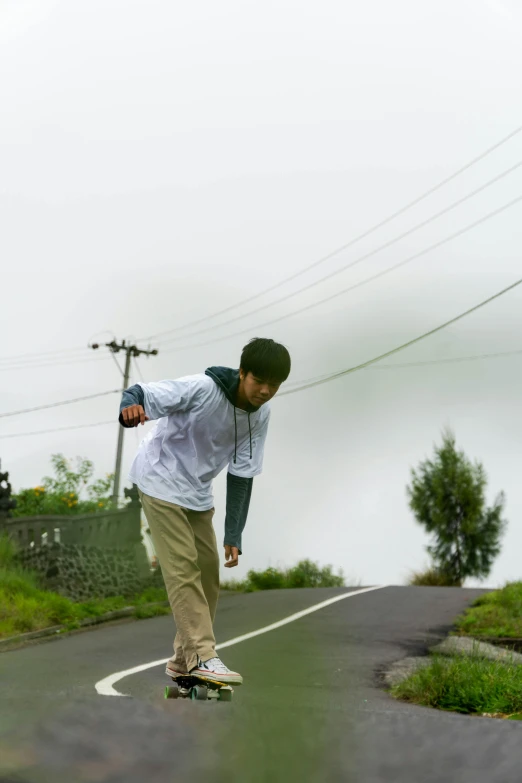 a boy in a white shirt riding a skateboard down a road